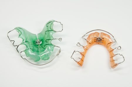 Links eine grüne, rechts eine orange herausnehmbare Zahnspange